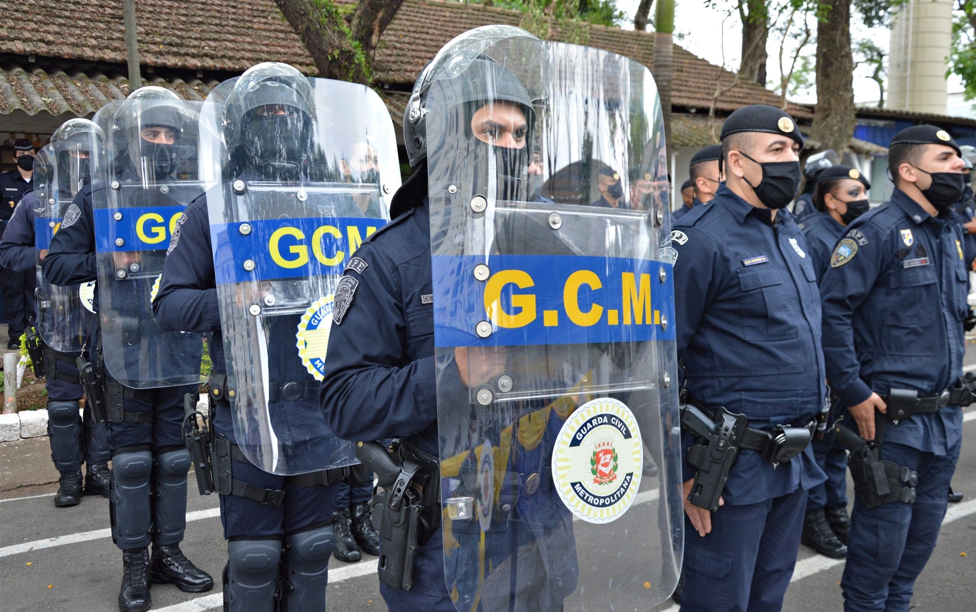 Guardas Civis Metropolitanos em formação, usando uniformes táticos e escudos de proteção. - Concurso GCM SP