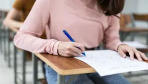 imagem de mulher sentada em carteira de sala de aula segurando caneta preenchendo gabarito - Concurso Prefeitura de Cascavel