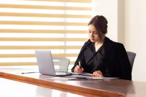 jovem empresária com roupa preta utilizando seu laptop, concentrada no trabalho do concurso TRF 5.