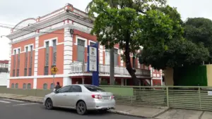 Sede da SEMEC em Teresina, Piauí, a distância. Parede em tom amarronzado, com janelas cinza e ao lado algumas árvores