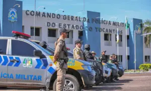 Policiais militares do Tocantins em frente a um edifício, com um carro de polícia ao fundo.