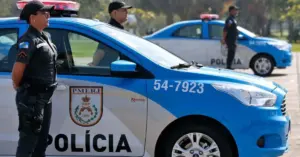 Policiais ao lado de uma viatura policial azul e branca / Concurso PMERJ