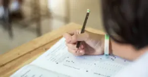 Estudante escrevendo com lápis em um papel durante uma prova na sala de aula / CNU