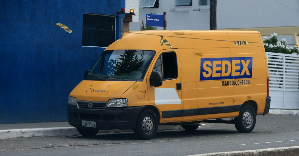 concurso Correios 2024. Veículo escrito Sedex na cor amarela e azul estacionado na rua.