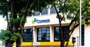 Fachada de um prédio dos Correios, com a logo da instituição e árvores em frente