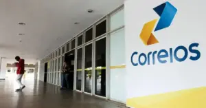 Fachada de uma das agências dos Correios com logo em parede e pessoas transitando em frente