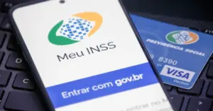 Celular sobre um cartão e sobre teclado de computador com a tela ligada no aplicativo do INSS