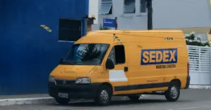 Veículo dos Correios Sedex na cor amarela e azul estacionado na rua