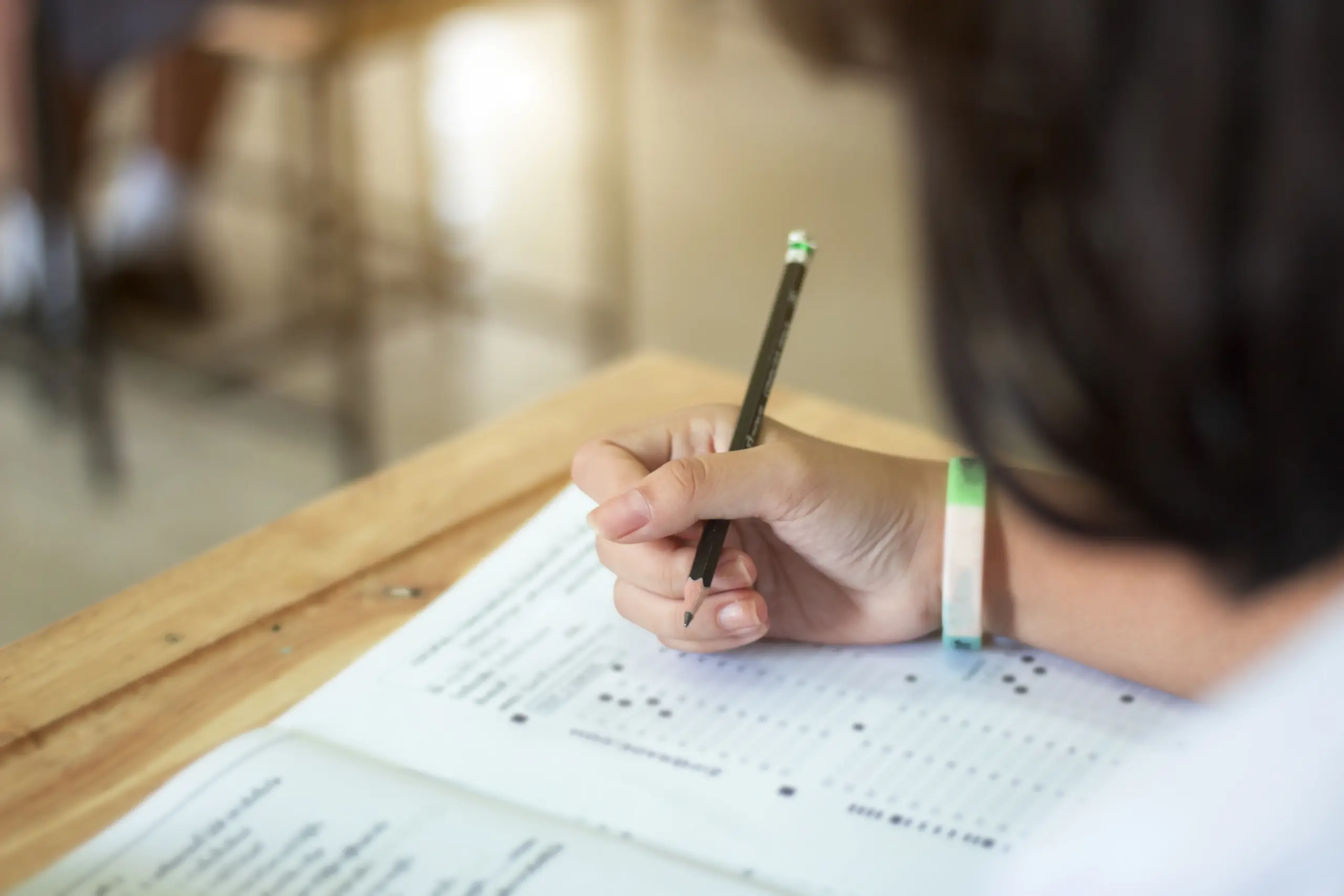 Estudante uniformizado escreve com um lápis em um papel durante uma prova em sala de aula.