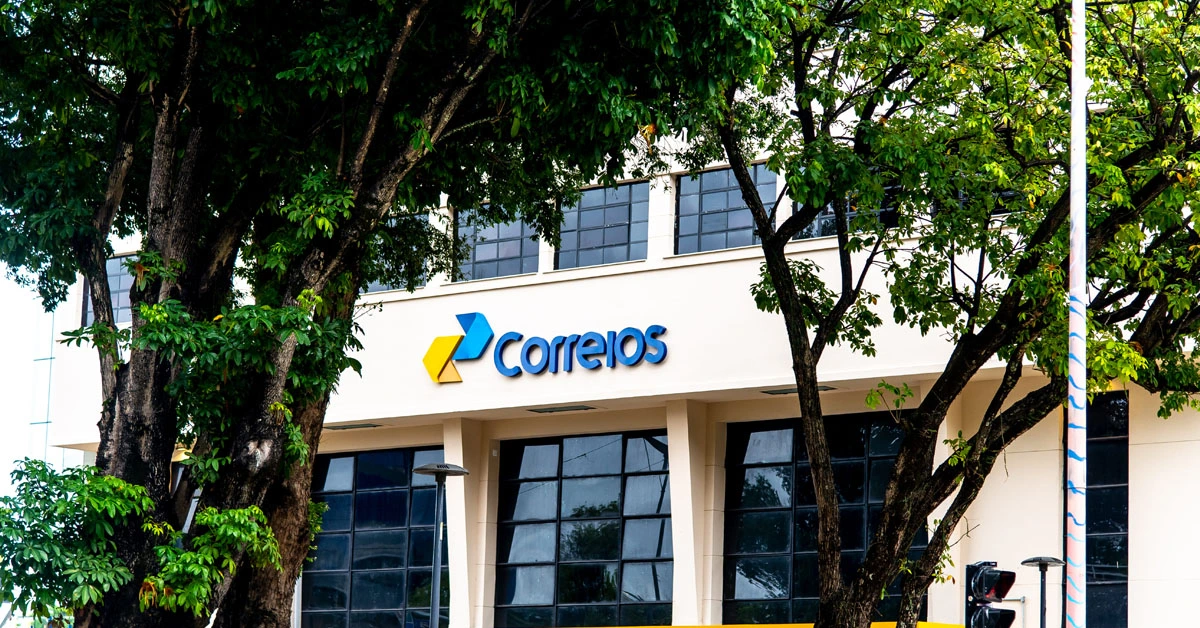 Fachada de um prédio dos Correios, com a logo da instituição e árvores em frente