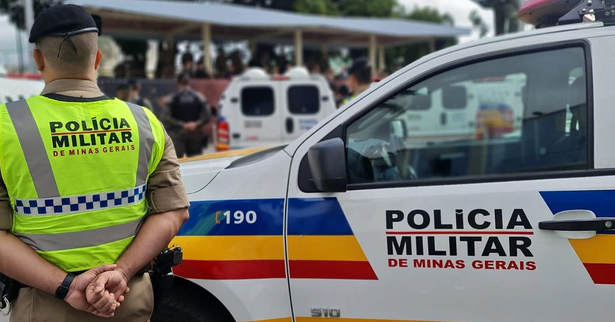 Agente da polícia militar ao lado de uma viatura da PM MG.