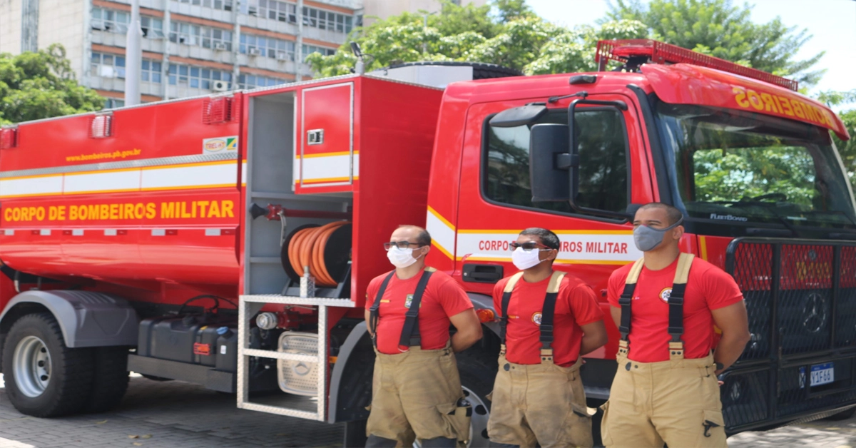 Caminhão do corpo de bombeiros estacionado e em frente oficiais da coorporação.