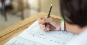 Pessoa em um ambiente de sala de aula preenchendo uma prova de múltipla escolha com um lápis / Concurso MPU