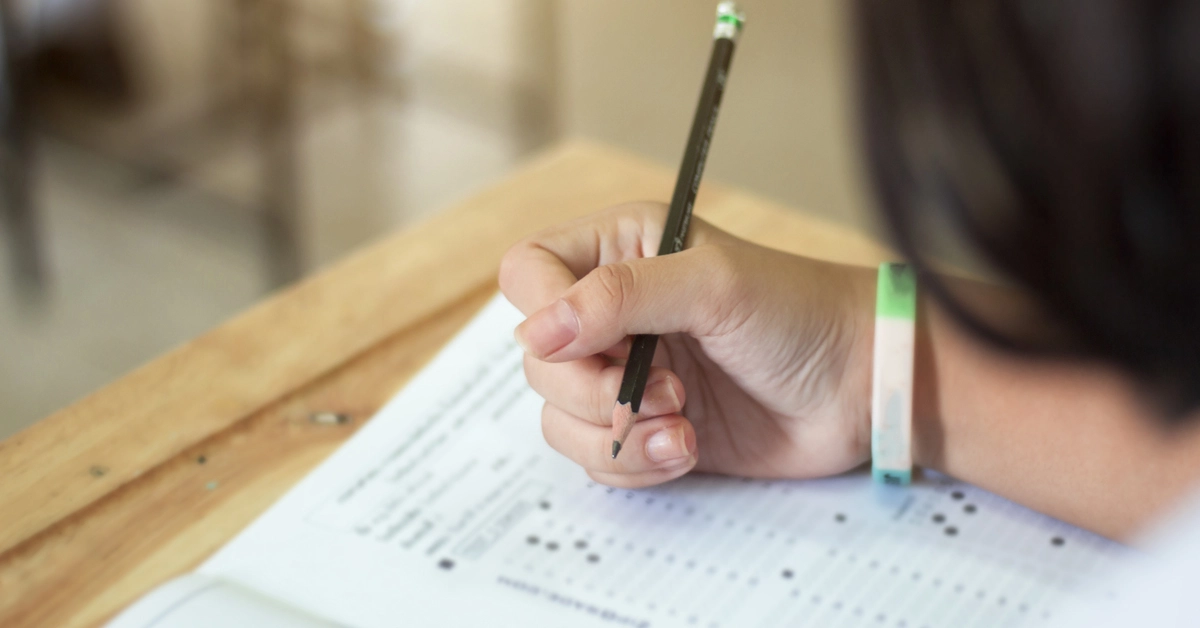 Pessoa em um ambiente de sala de aula preenchendo uma prova de múltipla escolha com um lápis / Concurso MPU