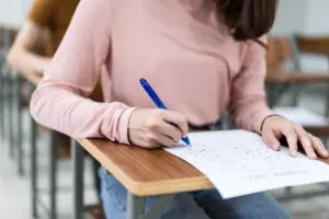 Concurso MPU. Uma pessoa sentada em uma mesa escrevendo em um pedaço de papel