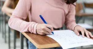 1. Mulher jovem escrevendo com caneta em uma folha de papel, concentrada em um exame em sala de aula.