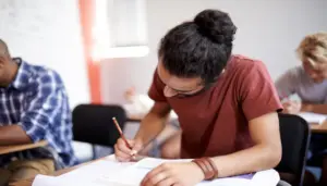 foto de um homem sentado em uma carteira de sala de aula segurando lápis e preenchendo gabarito do Concurso Prefeitura de Araucária PR