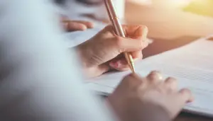 imagem de uma mulher segurando uma caneta dourada escrevendo em um caderno de provas do Concurso Segurança RS