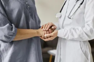 imagem de uma mulher de jaleco branco e estetoscópio segurando a mão de uma paciente - Concurso SES SE