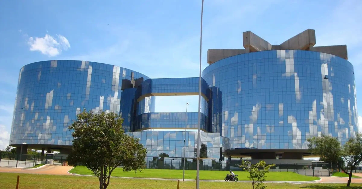 Prédio espelhado do Ministério Público da União sob um céu azul, refletindo a luz / Concurso MPU