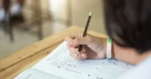 Uma pessoa está segurando um lápis enquanto preenche um formulário em uala de aula / Concurso MPU