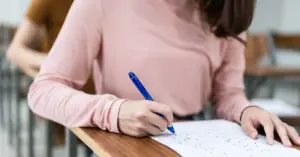 Mulher sentada em carteira de sala de aula segurando caneta preenchendo gabarito / Concurso Funpresp-Exe