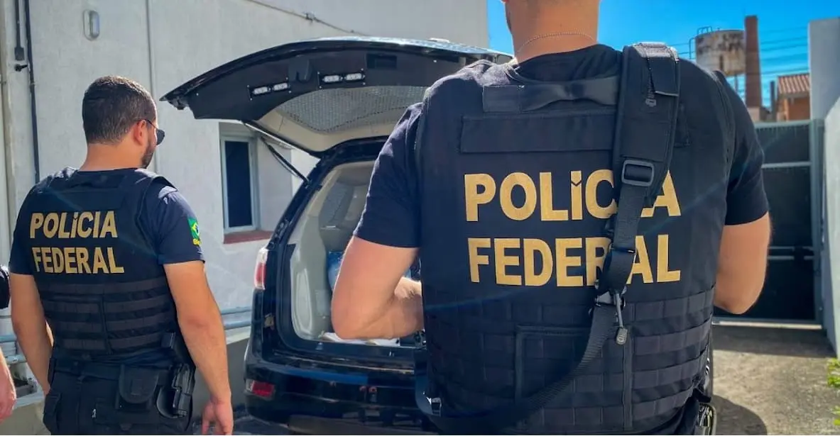 dois policiais federais de costas olhando porta malas do carro aberto