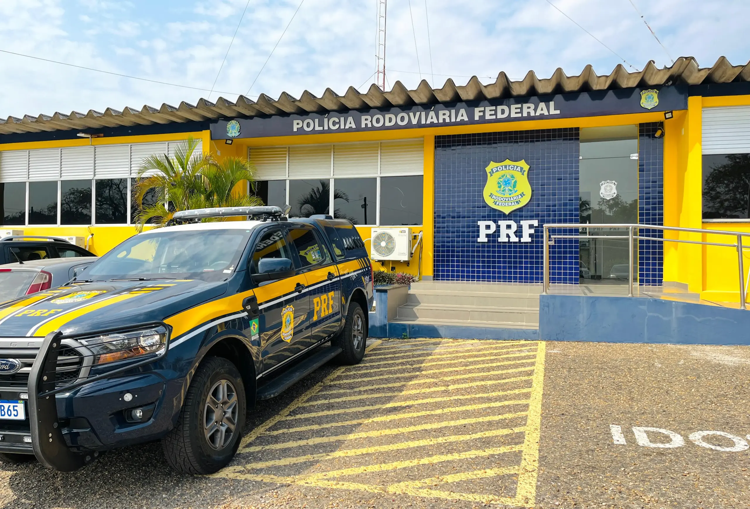 Entrada da Polícia Rodoviária Federal em um dia ensolarado e com uma viatura policial estacionada na frente.