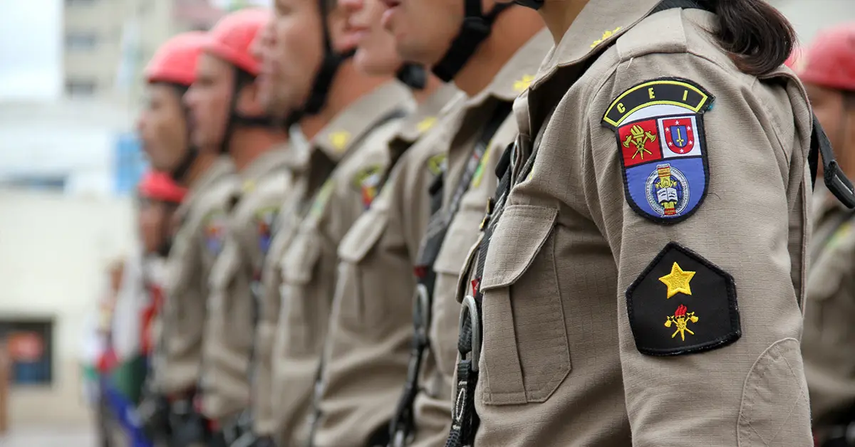 Fila de bombeiros militares uniformizados, usando capacetes vermelhos / Concursos PM PR e Bombeiros PR