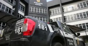 No primeiro plano, um veículo preto oficial da Polícia Civil e ao fundo um prédio da Polícia Civil / Concurso PC BA