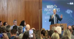 Uma sala cheia de pessoas em um evento e um painel azul exibe o texto "Mais Professores para o Brasil" / CNU dos professores