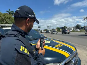 Polícial Rodoviário Federal em frente ao carro do concurso PRF falando no telefone