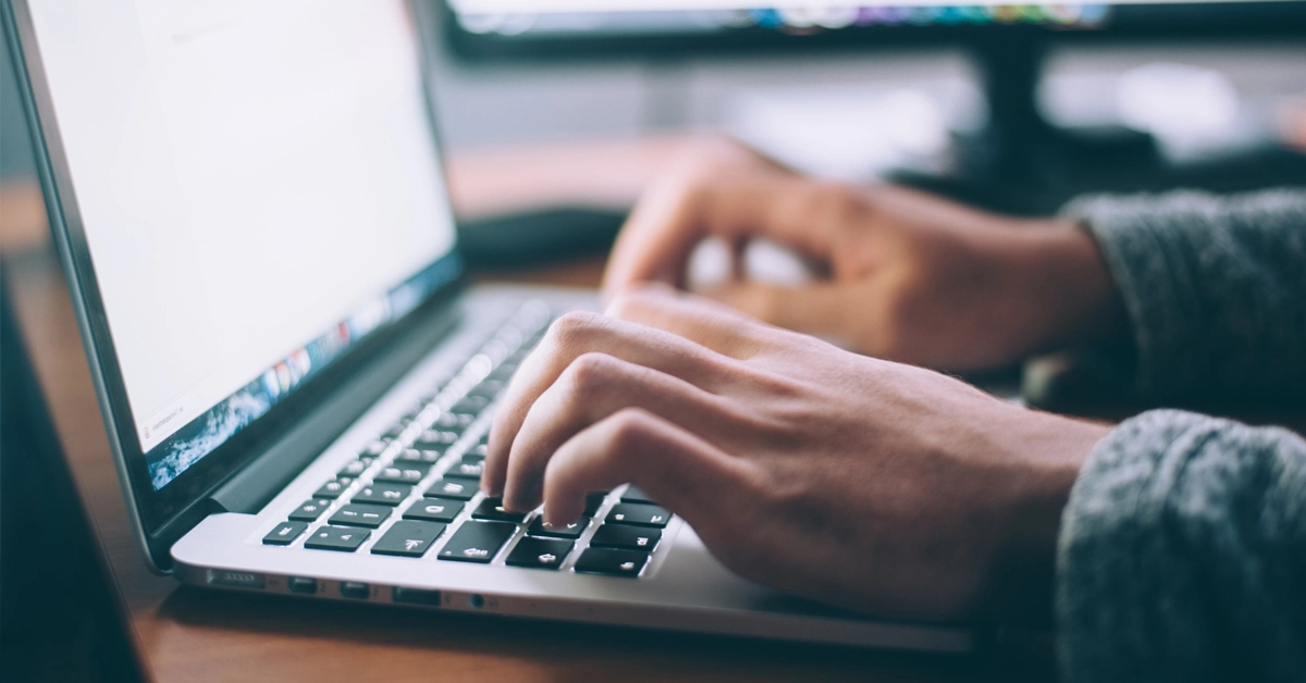 Mãos digitando em notebook com tele ligada / Concurso Susep