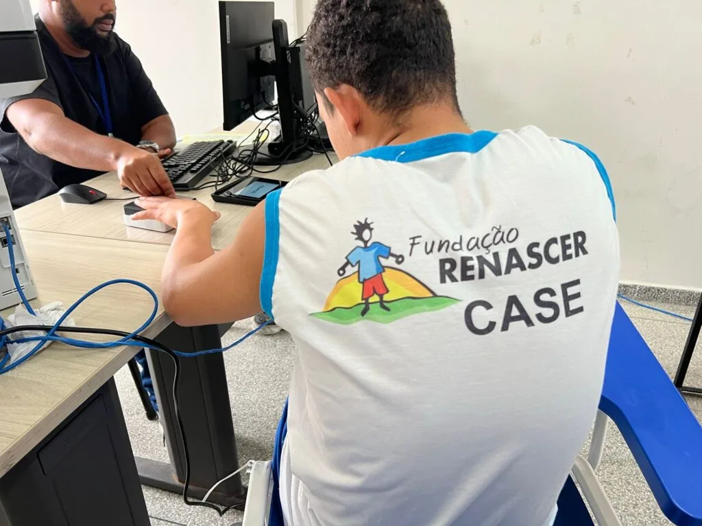 Um homem sentado realizando a coleta da digital de um interno da Fundação Renascer