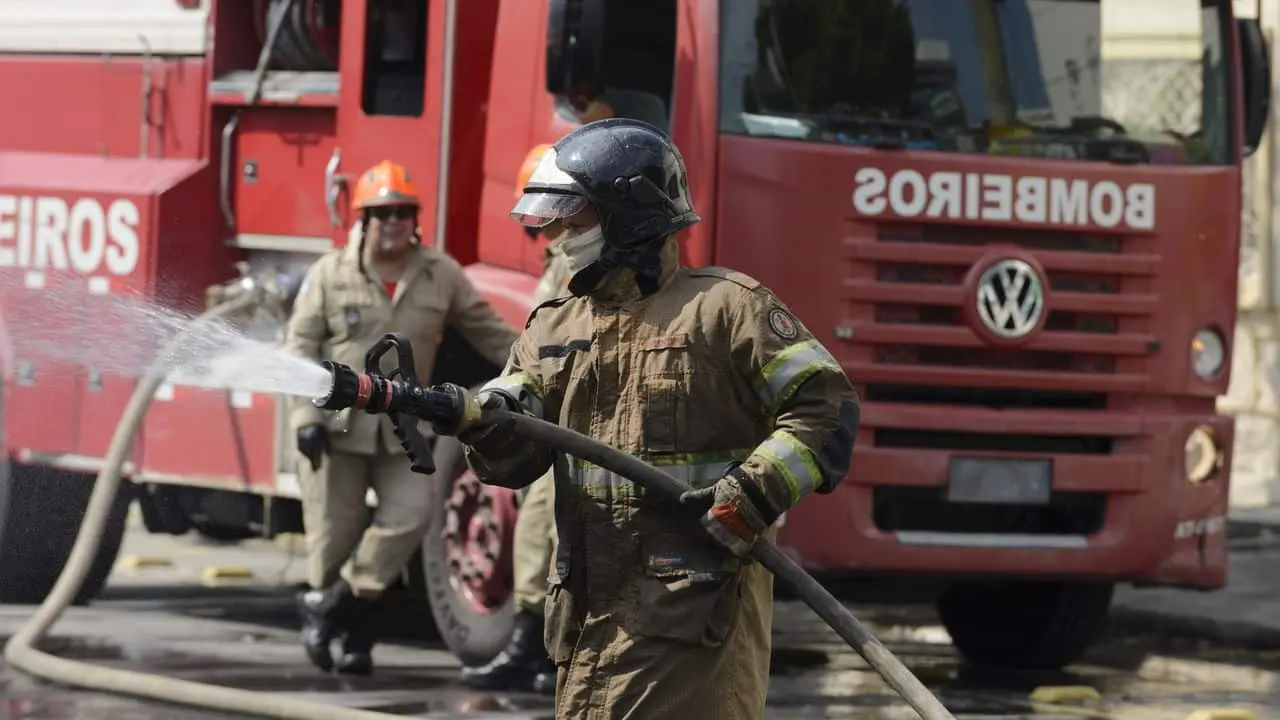 Bombeiro em ação com mangueira de alta pressão durante simulação. – Concurso Bombeiros RS